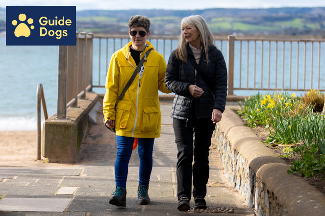 A sight impaired woman being led by another woman who is a sighted guide volunteer.